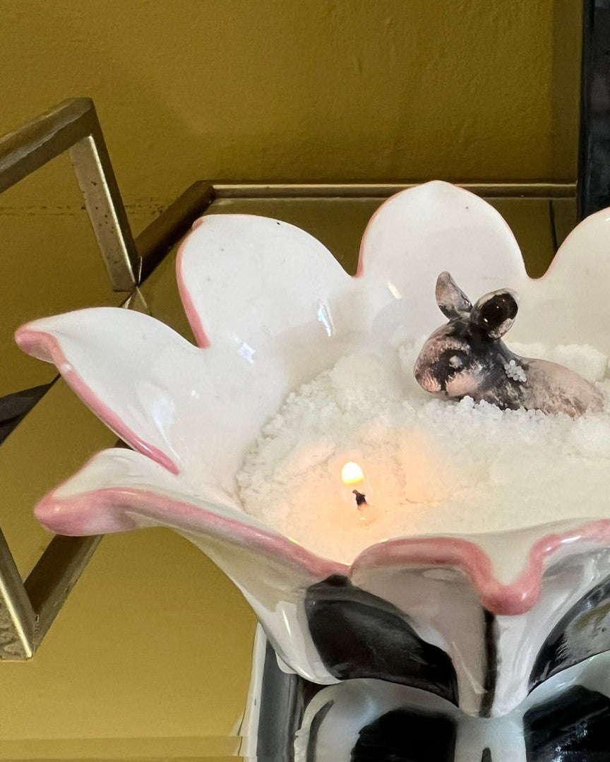 Small animal in a decorative ceramic bowl with a candle inside on a yellow surface.