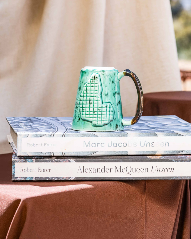 Stack of books with a green mug on top, placed on a table outdoors.