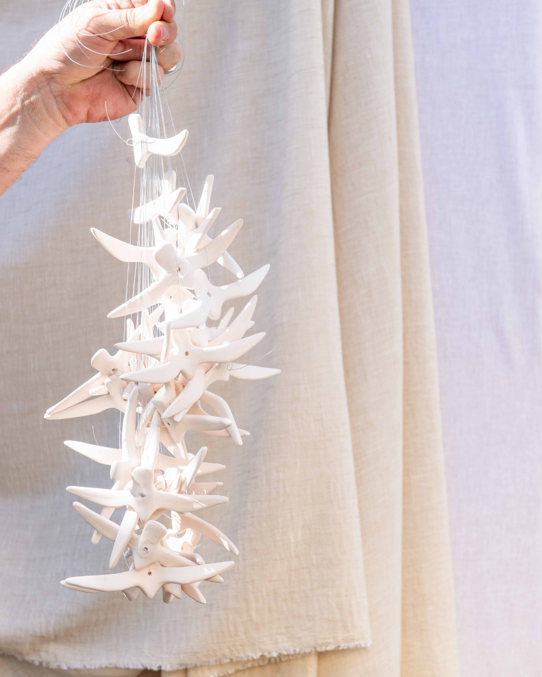 Hand holding a decorative item made of white starfish against a light background