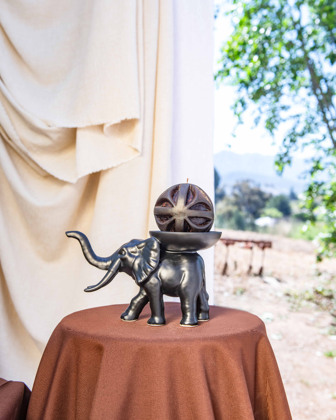 Decorative elephant sculpture with a spherical candle object on a round table outdoors.