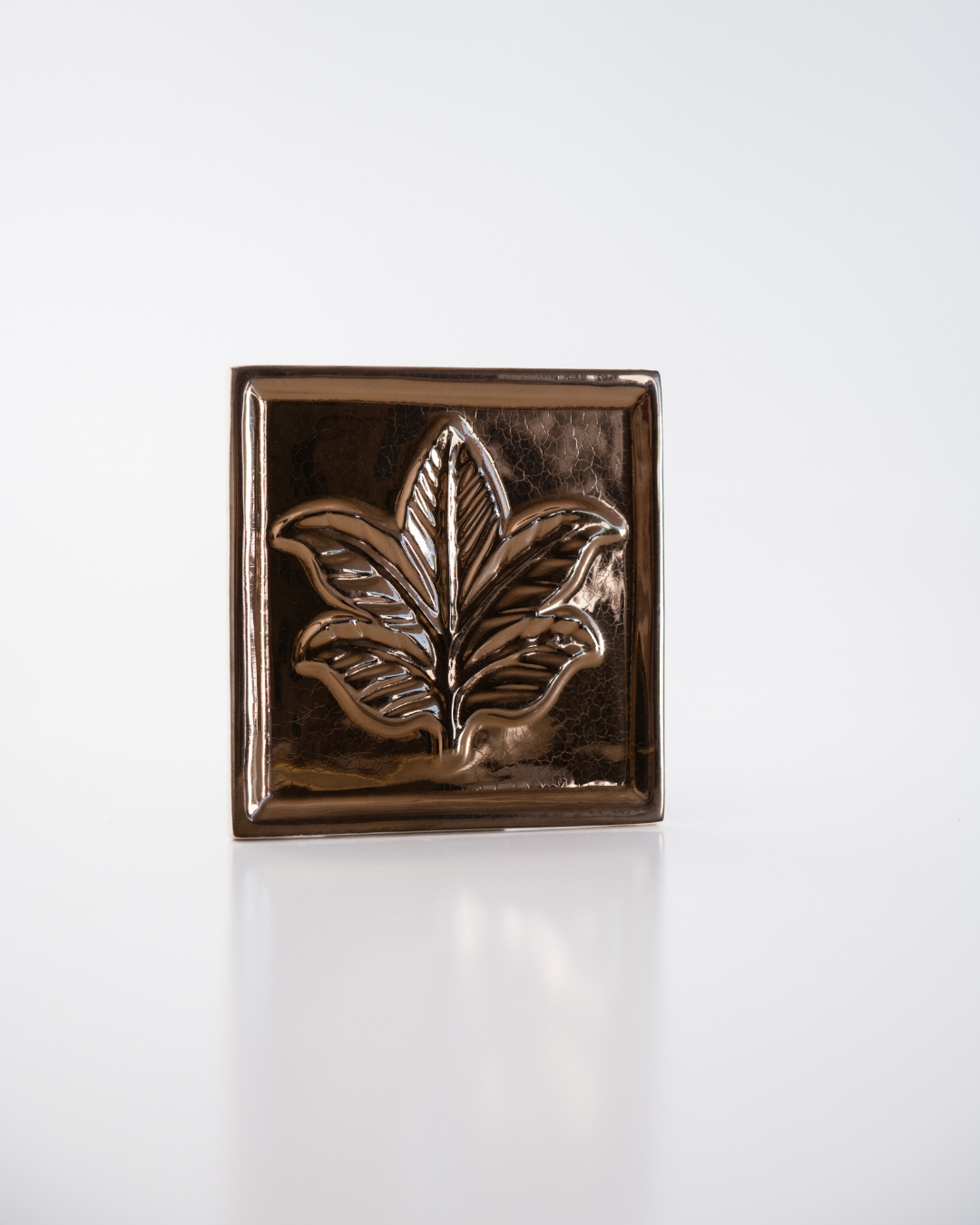 Bronze decorative tile with leaf design on a white background