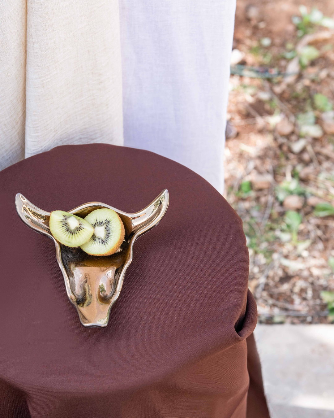 Decorative Bronze ceramic bull head vessel with sliced kiwis on a brown surface outdoors.