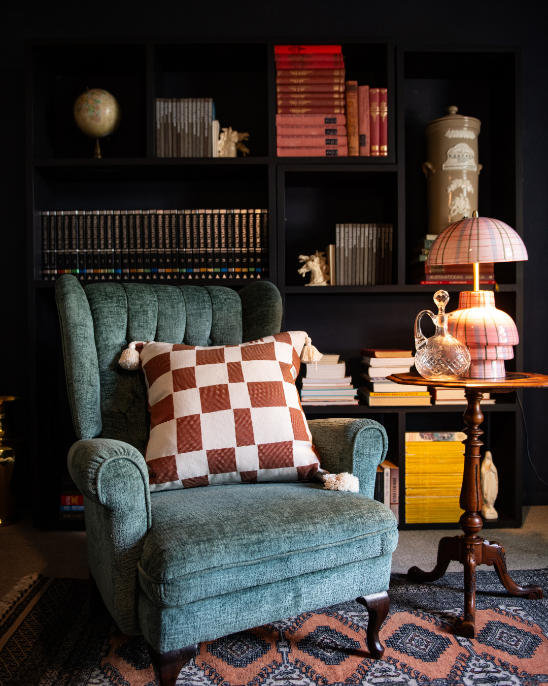 Cozy living room with a teal armchair, checkered pillow, and bookshelf.