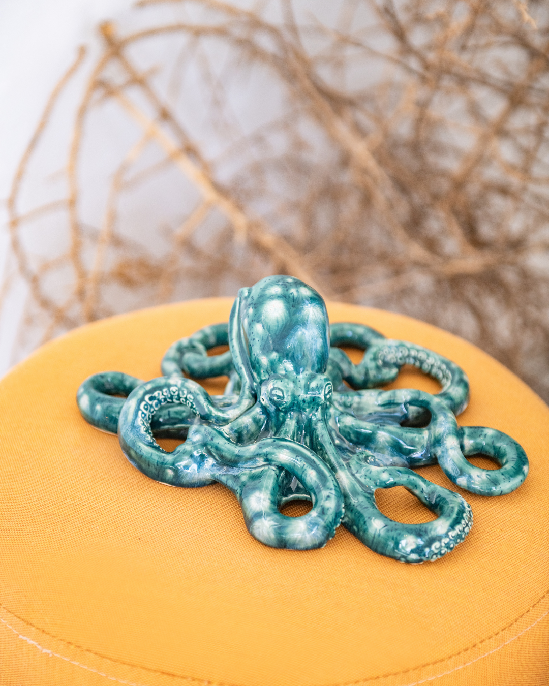 Teal ceramic octopus on a yellow surface with a blurred natural background