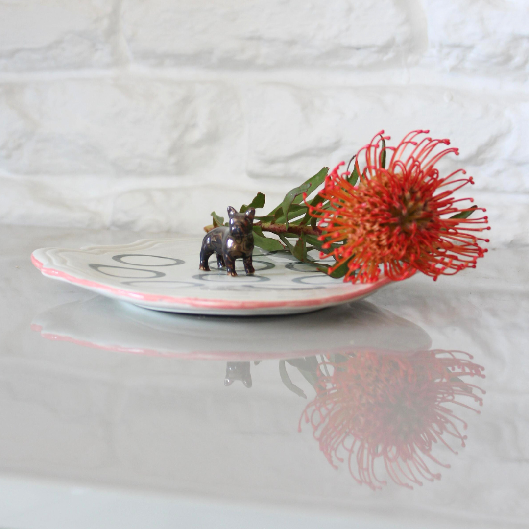 Small figurine of a dog next to a red flower on a white plate with a blurred background