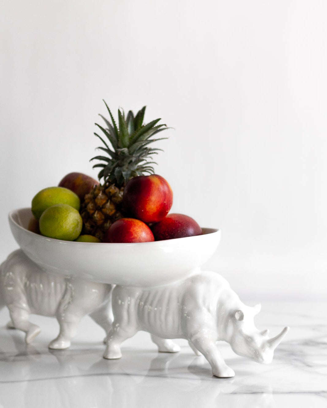 Fruit bowl with a pineapple, apples, and other fruits on a decorative stand with rhino design.