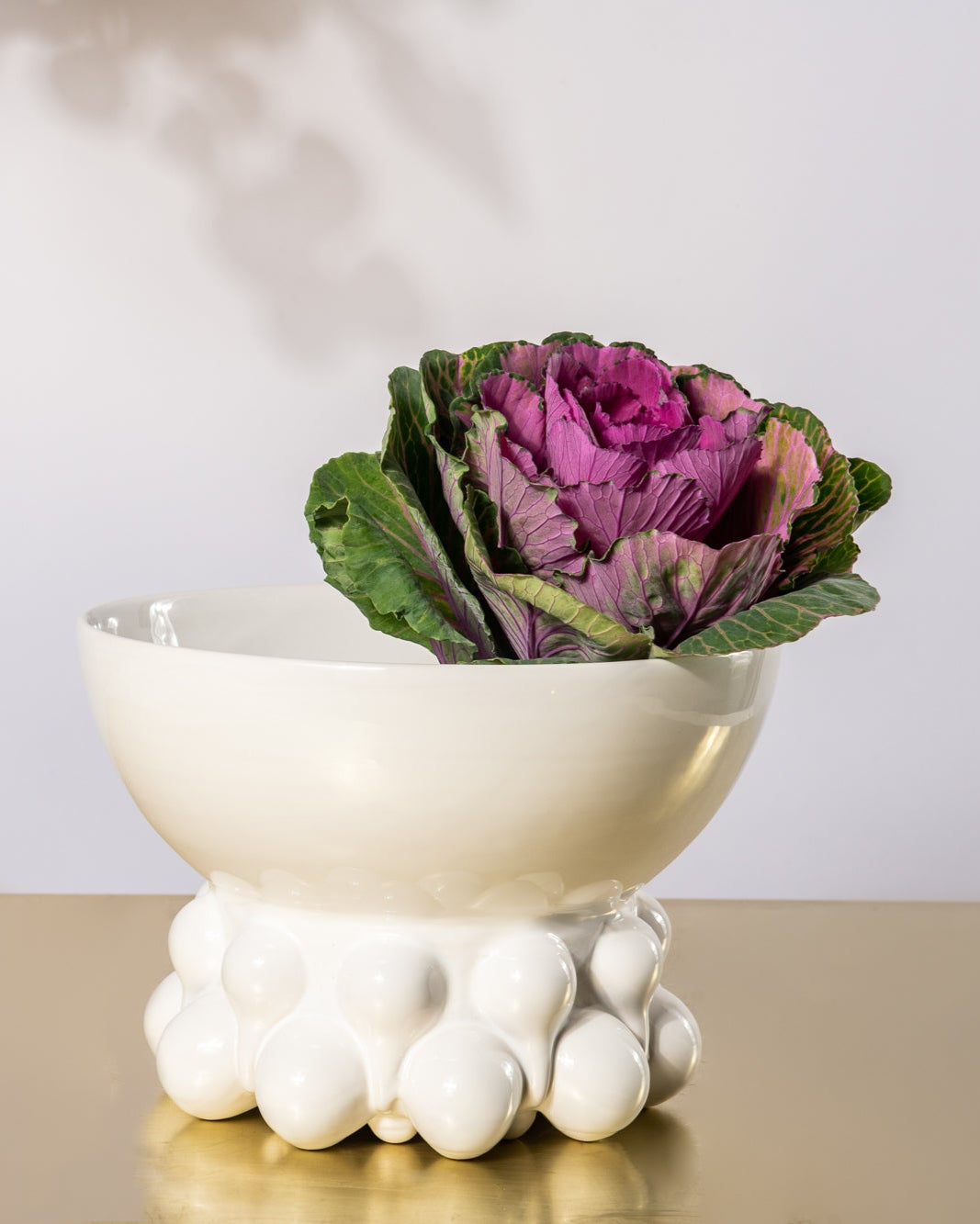 White decorative bowl with a purple and green cabbage-like plant on a wooden surface.