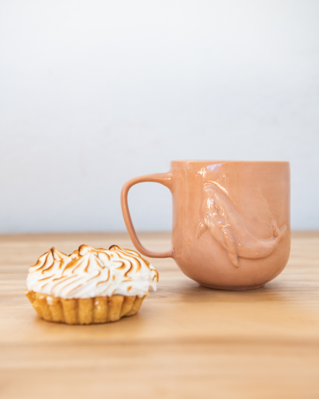 Ceramic mug with a unique design on a wooden surface next to a dessert.