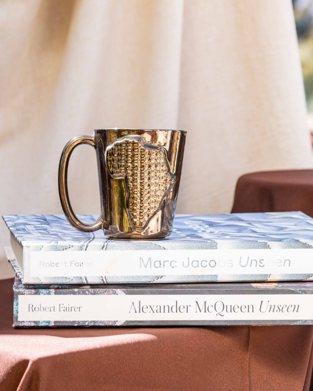 Gold mug on a stack of books with a beige curtain and outdoor view in the background