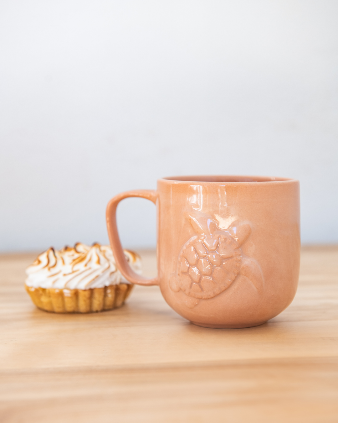 Ceramic mug with turtle design on a wooden surface next to a dessert.