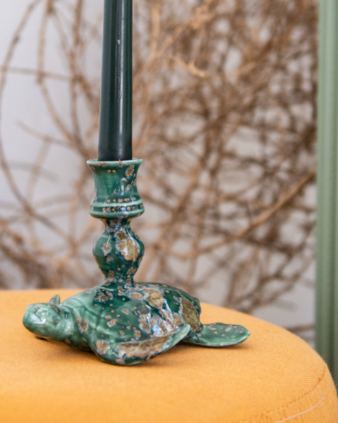 Decorative Crystal Jade sea turtle candle stick holder including a green candlestick, on an orange cushion against a white wall.