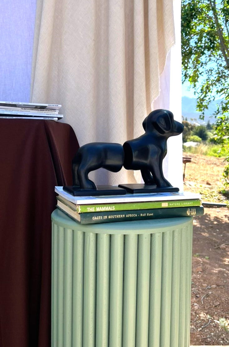 Black dog figurine on books on a green pedestal with outdoor background