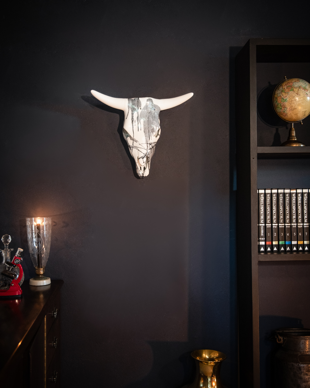 Decorative bull skull on a dark wall with a bookshelf and globe in the background