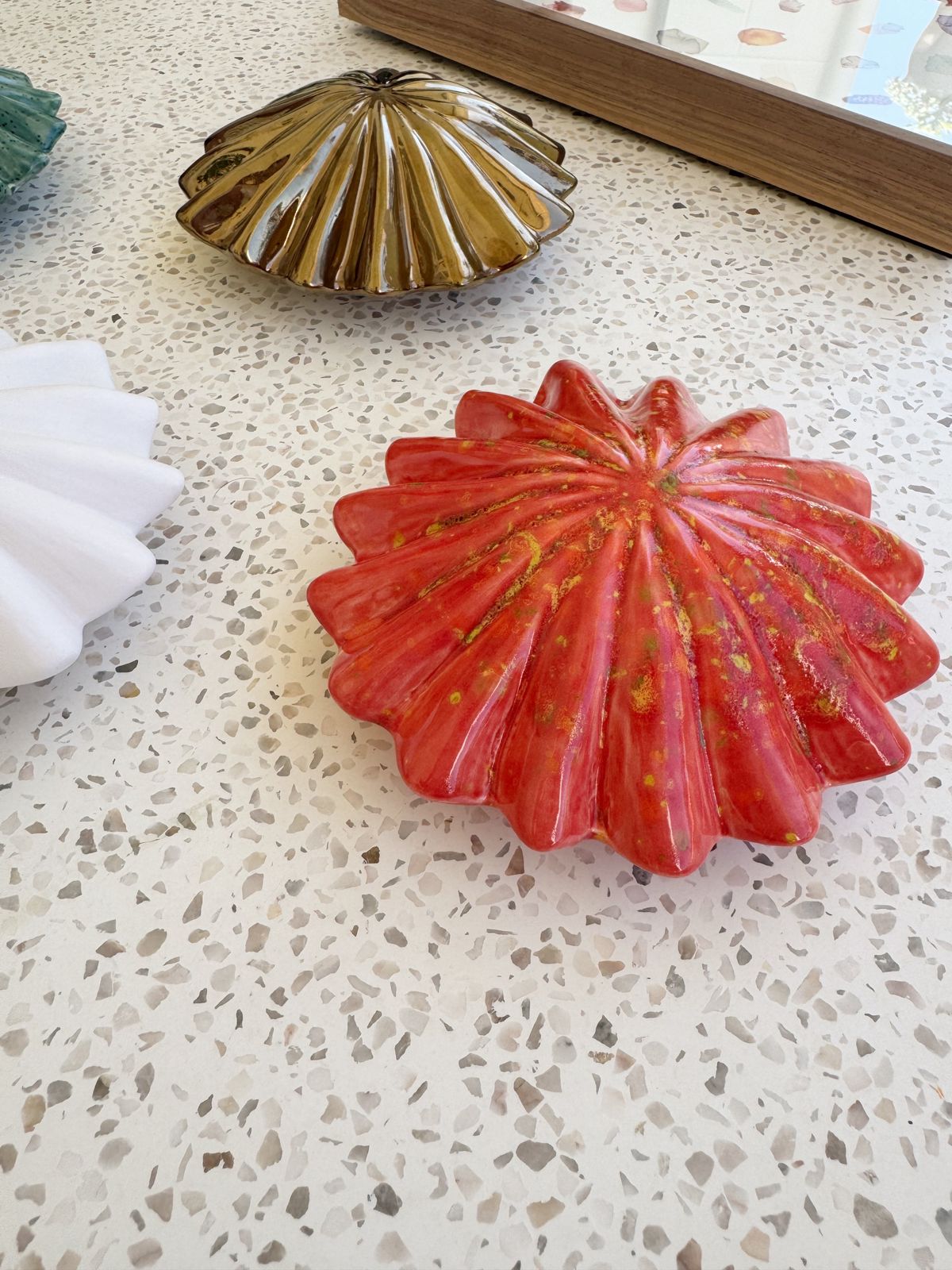 Red seashell-shaped object on a textured surface with another shell in the background.