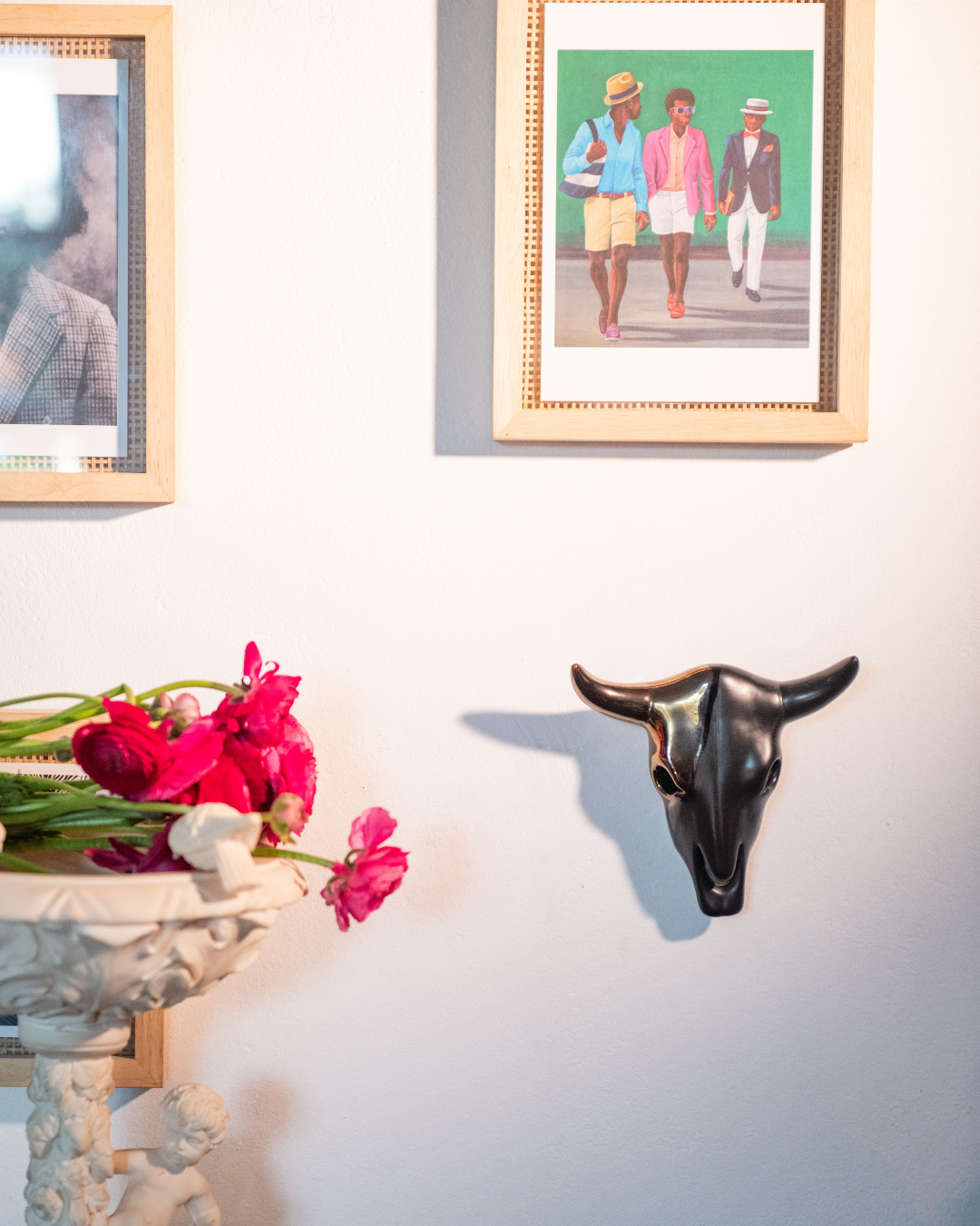Decorative bull head on a wall with framed pictures and flowers below.