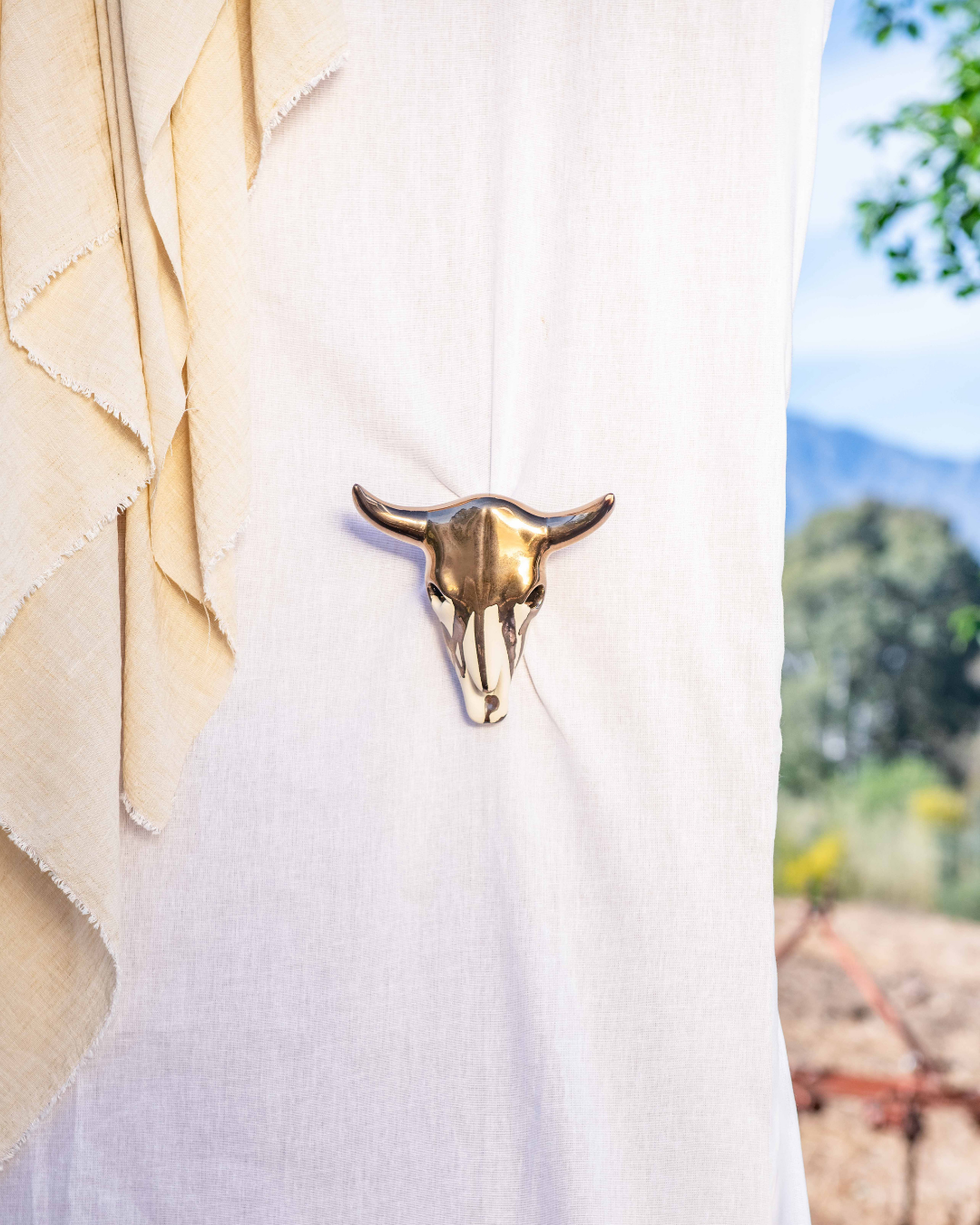 Brass cow head ornament on a white shirt with a blurred outdoor background