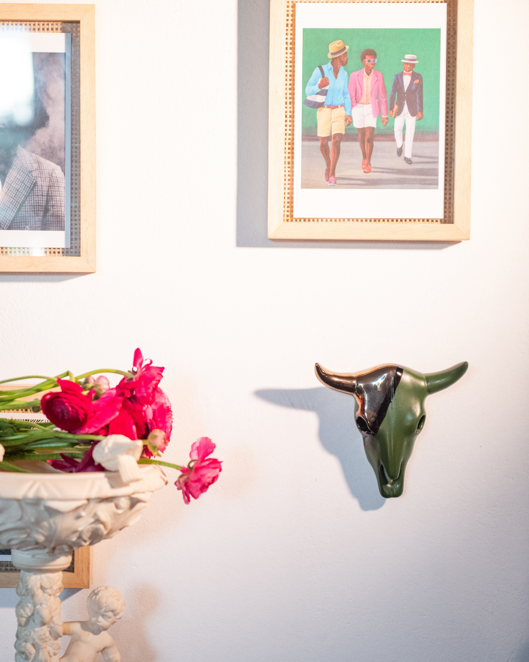 Decorative wall with framed pictures, a ceramic bull head, and flowers.