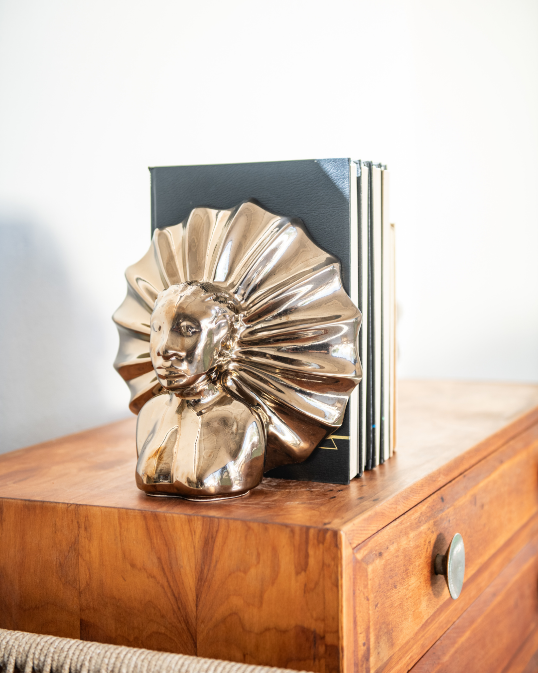 Decorative bookends shaped like a face with feathers on a wooden surface.