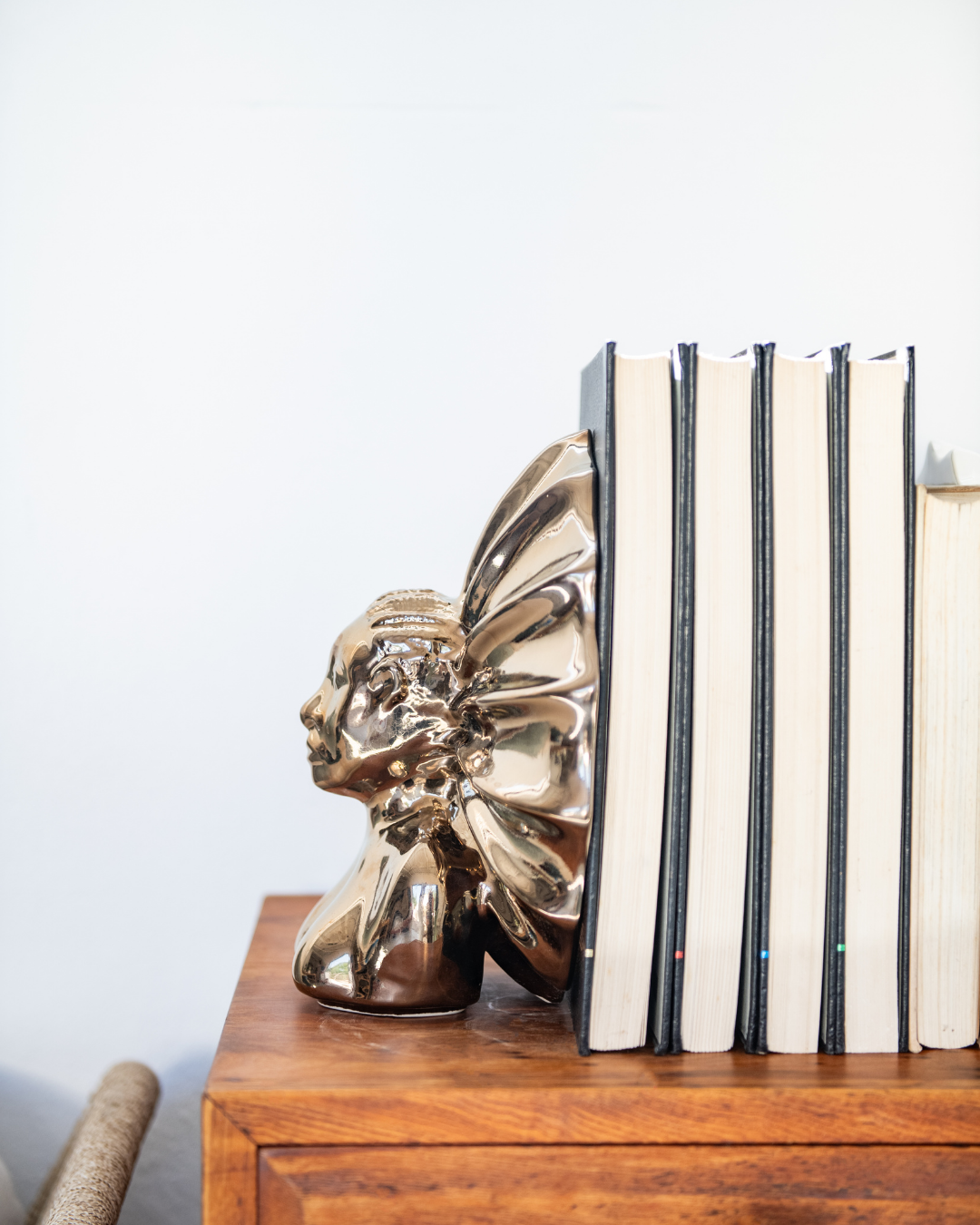 Gold head-shaped bookend next to striped books on a wooden surface with a light gray background