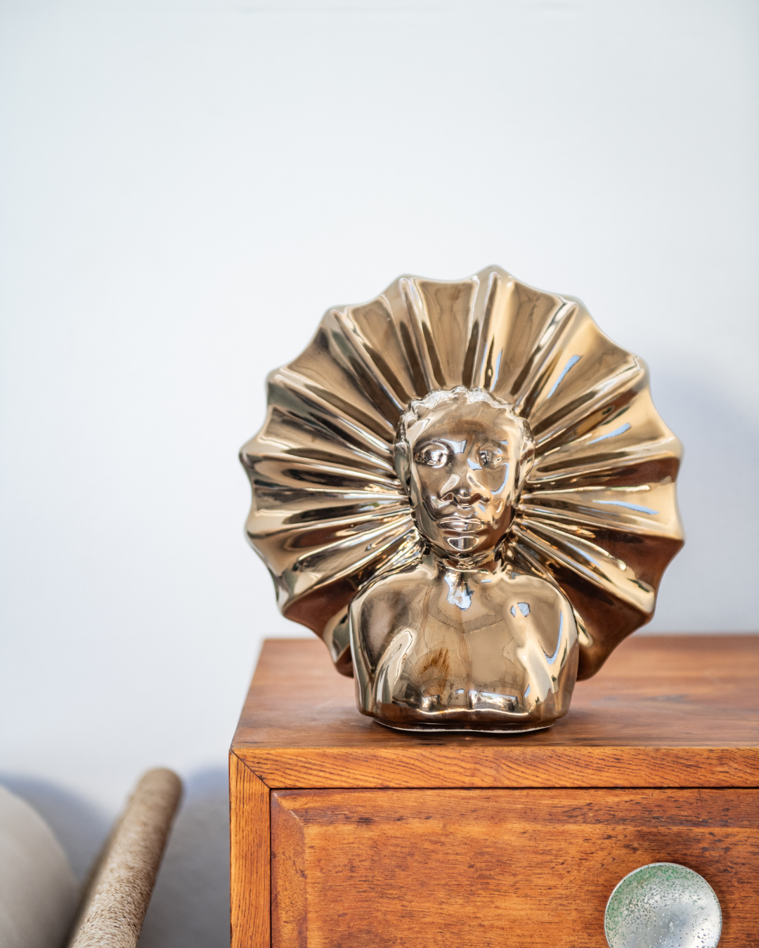 Gold bust sculpture on a wooden surface with a light gray background