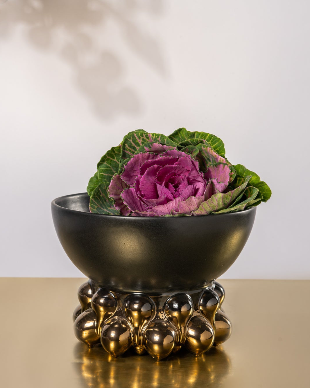 Decorative black bowl with a pink flower on a gold stand against a white background