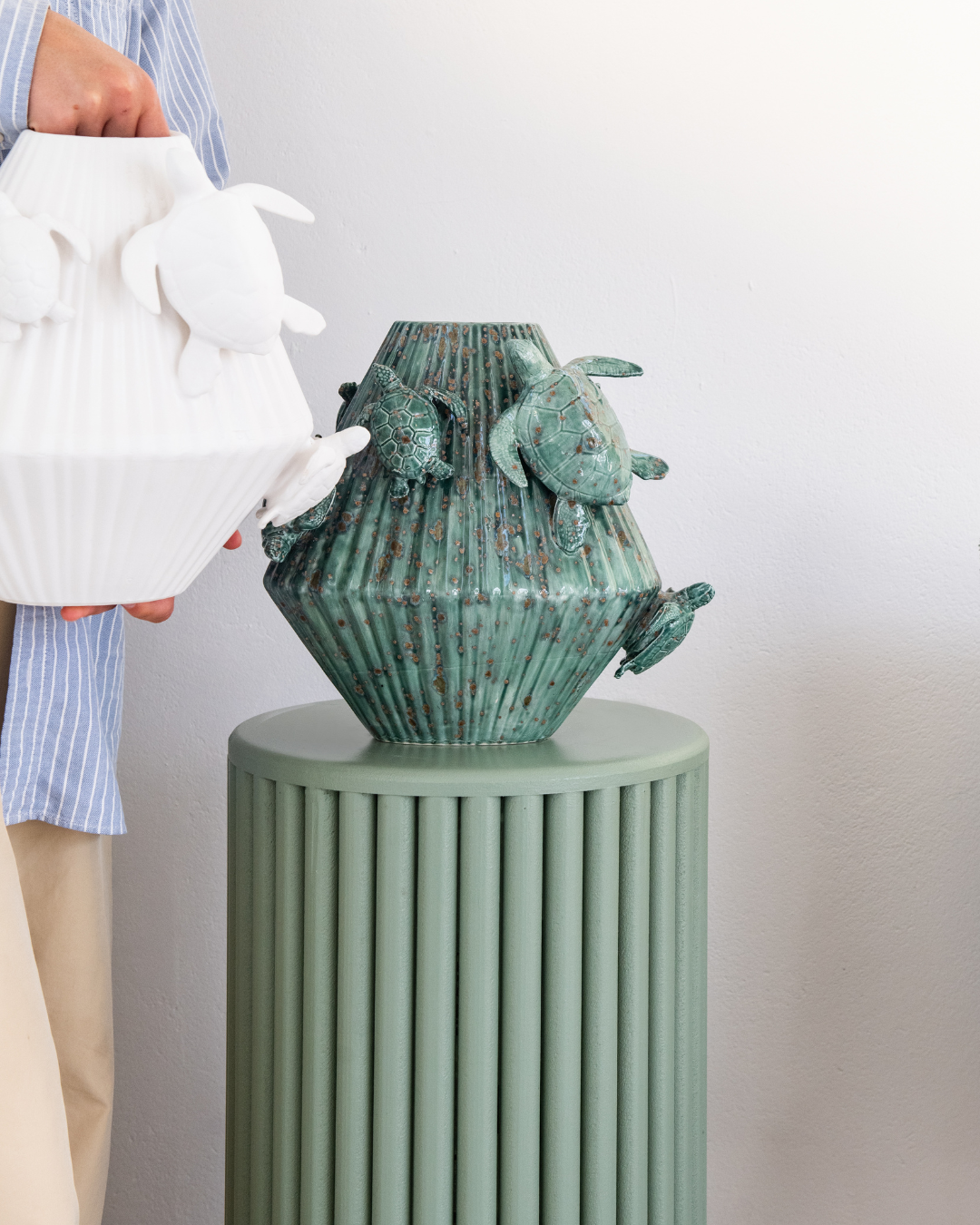 Green & Matt White decorative vase with 3d sea turtles attached on a matching pedestal with a person holding a white version in the background