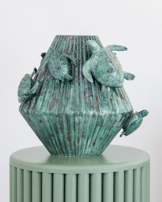 Green & Matt White decorative vase with 3d sea turtles attached on a matching pedestal with a person holding a white version in the background