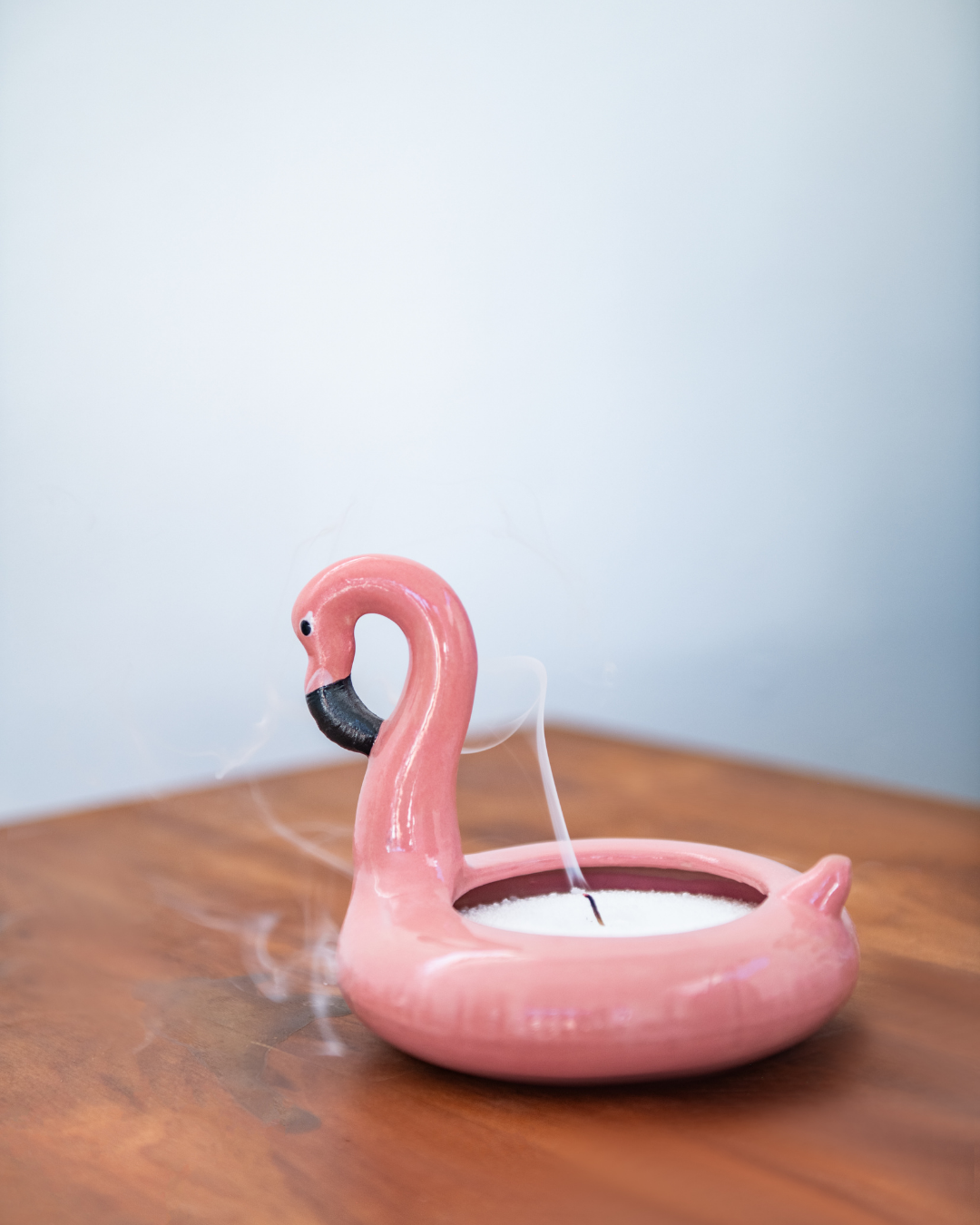 Pink flamingo-shaped candle holder on a wooden surface with a light blue background