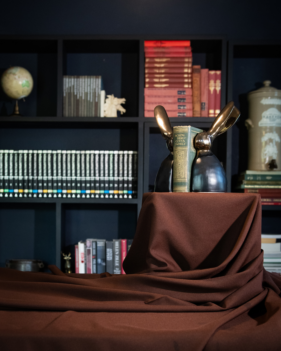 A Riverine Rabbit Book end in Black and Bronze on a brown cloth with a bookshelf in the background