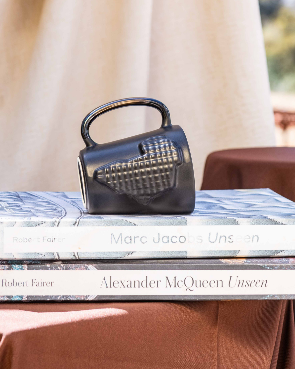Stack of books on a table with a black ceramic mug on top, against a beige curtain backdrop.