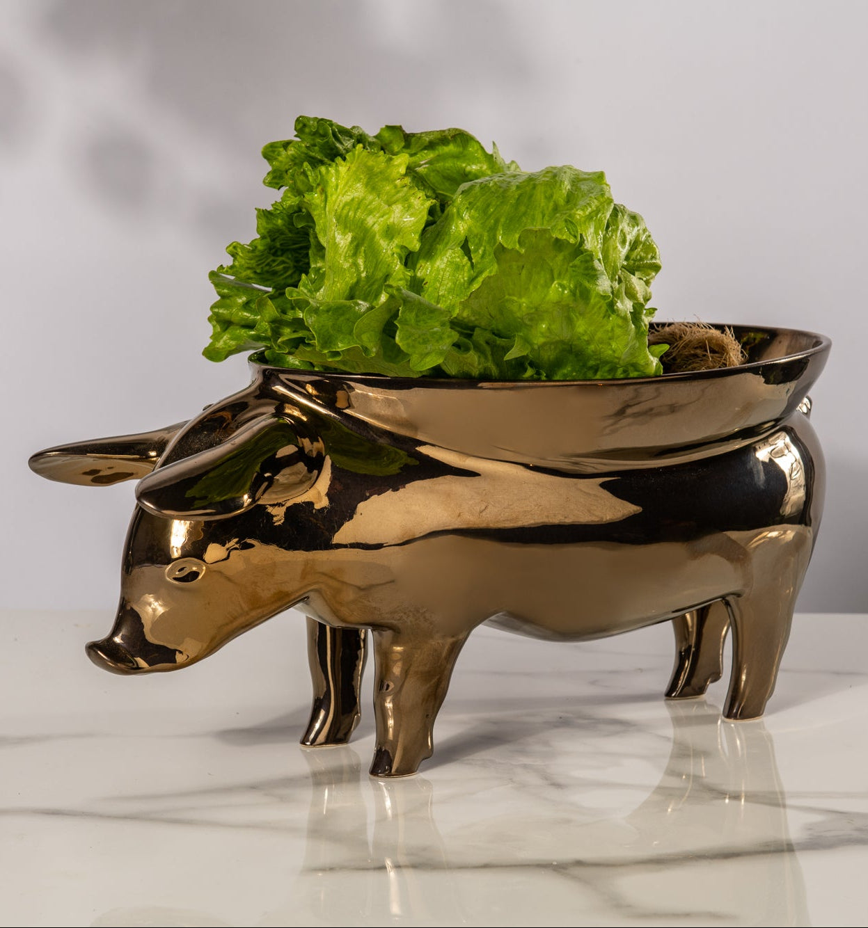 Gold pig-shaped bowl with green lettuce on a marble surface