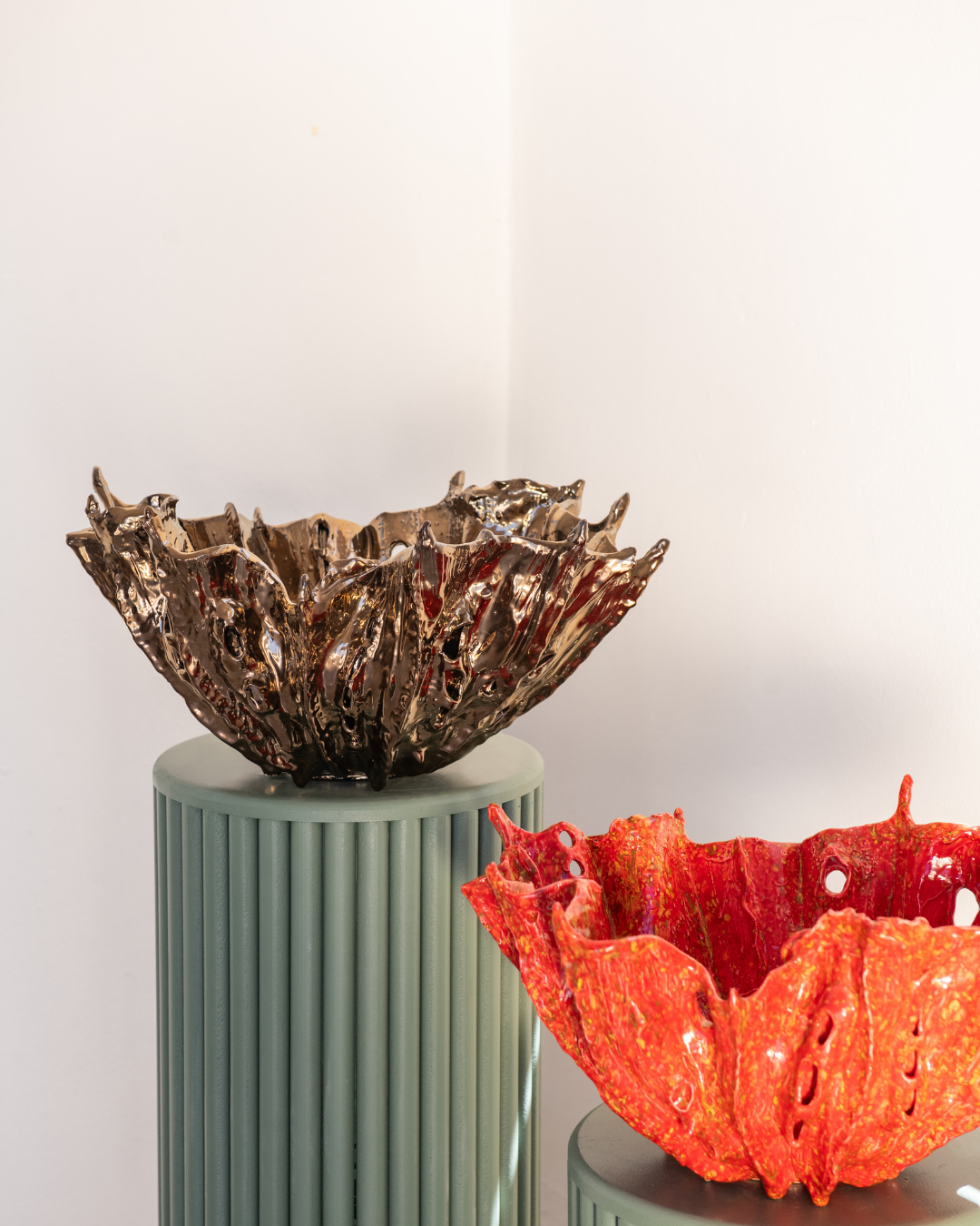 Two unique ceramic bowls, one metallic brown and one red, on cylindrical stands against a light background.