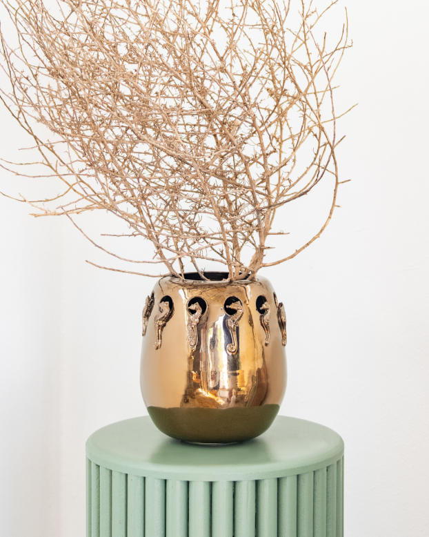 Bronze Rialheim vase with dried branches on a green pedestal against a white background