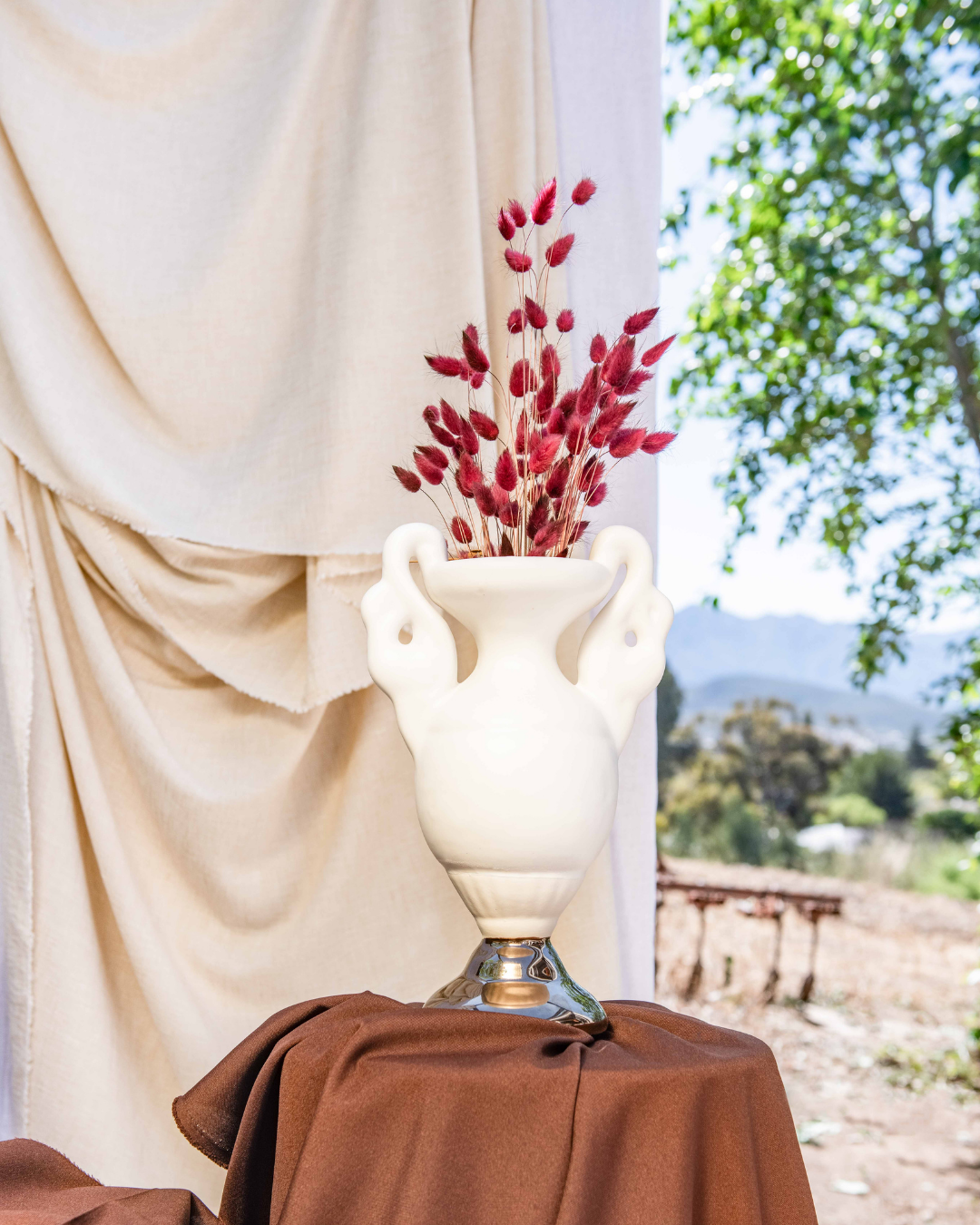 Decorative vase with red flowers on a table with a draped cloth, outdoor setting