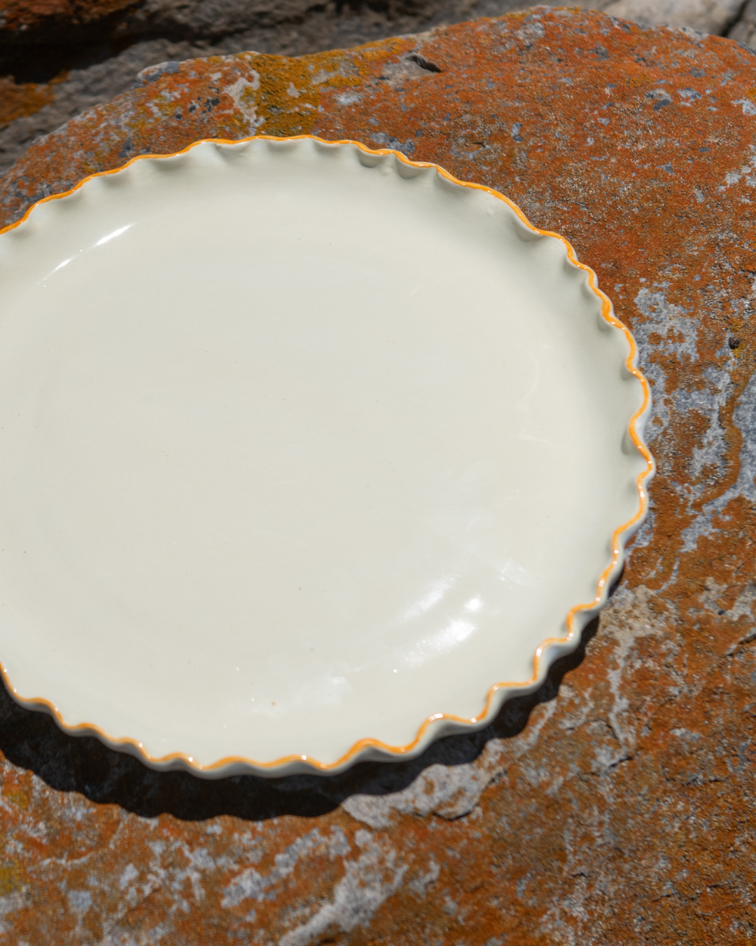 White ceramic dinner plate with scalloped edge on a textured brown surface