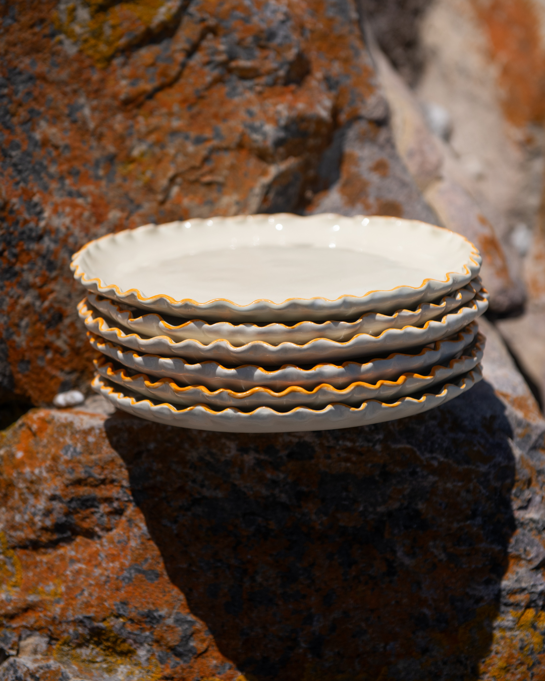 Stack of ceramic plates with scalloped edge on a textured stone surface