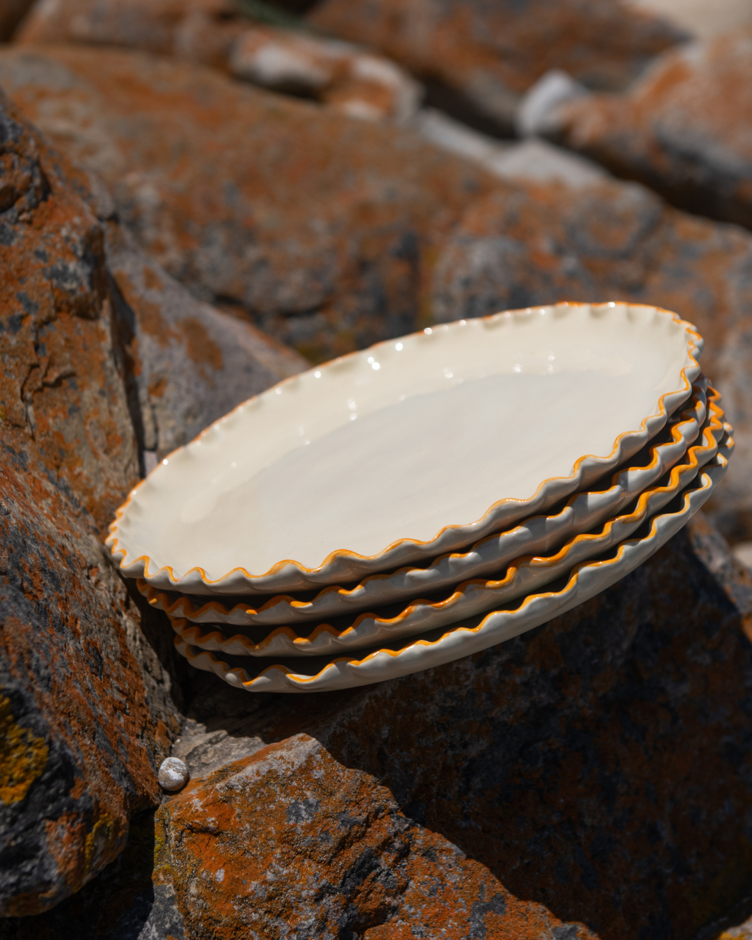 Stack of ceramic plates with coral rim on a textured stone surface