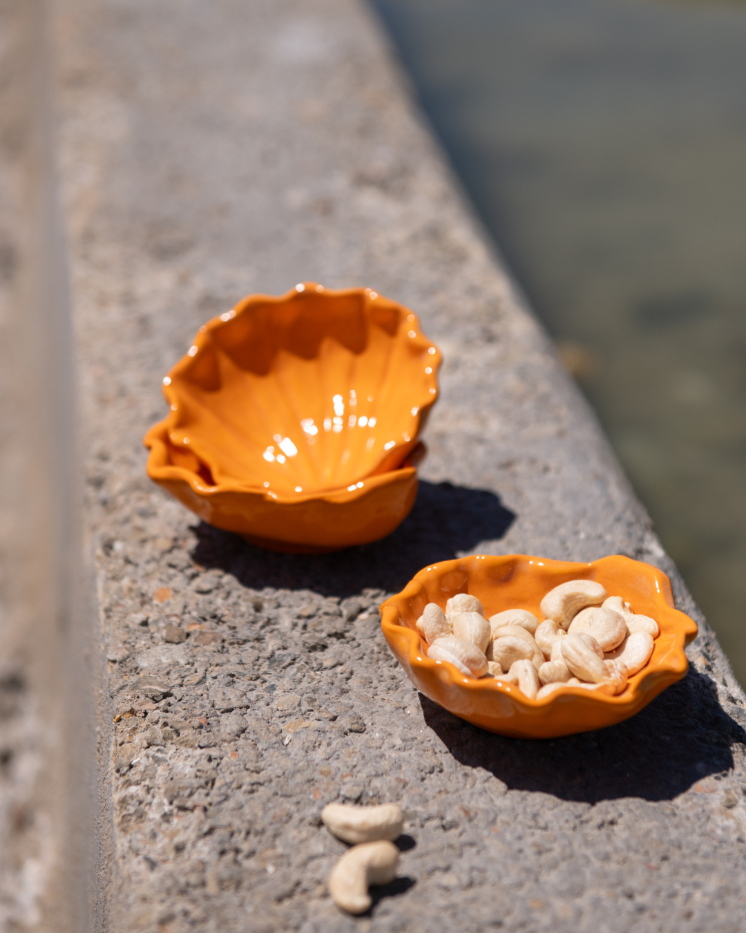 Two orange ceramic bowls on a concrete surface with water in the background