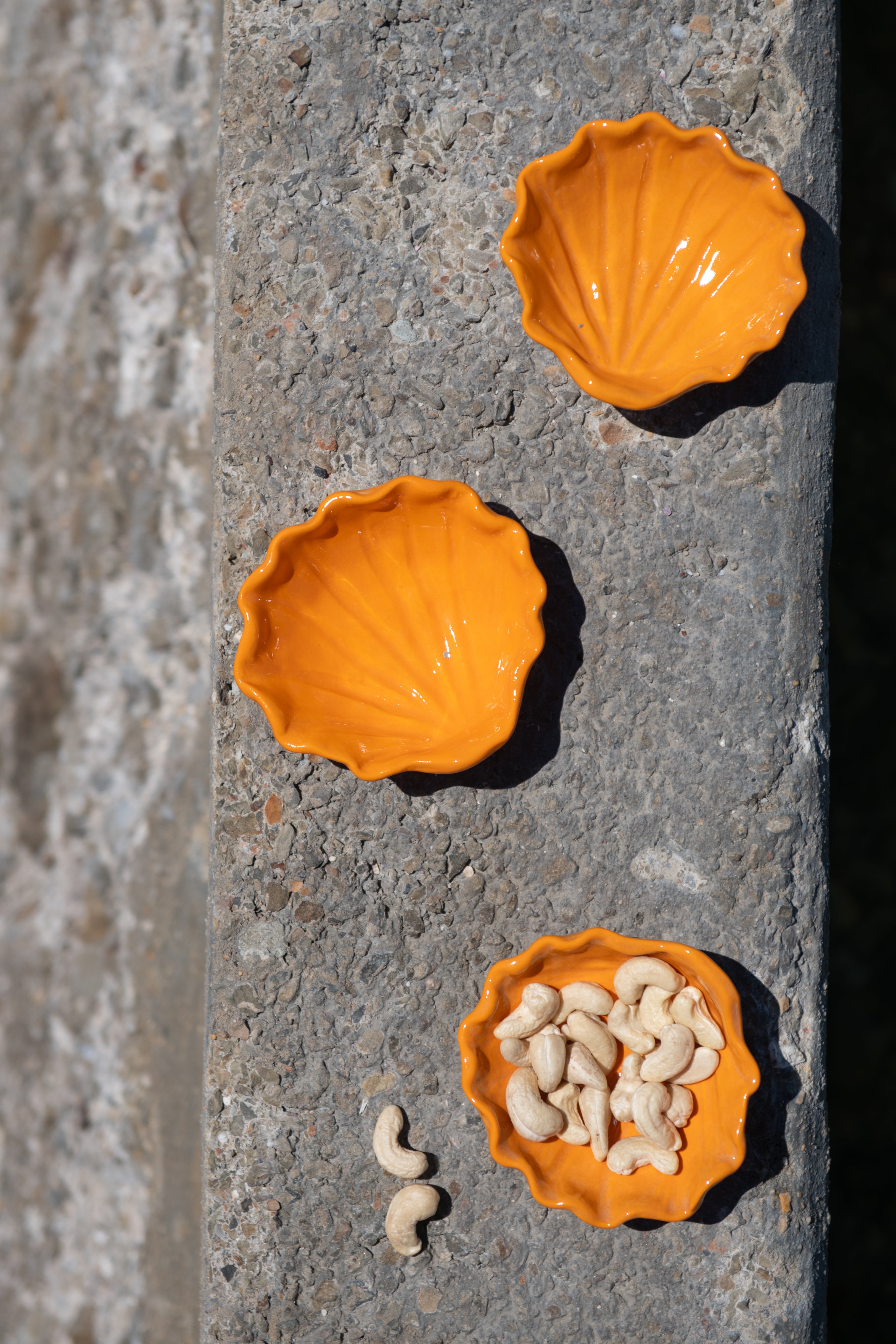 Three orange ceramic bowls on a stone surface with one containing small objects.