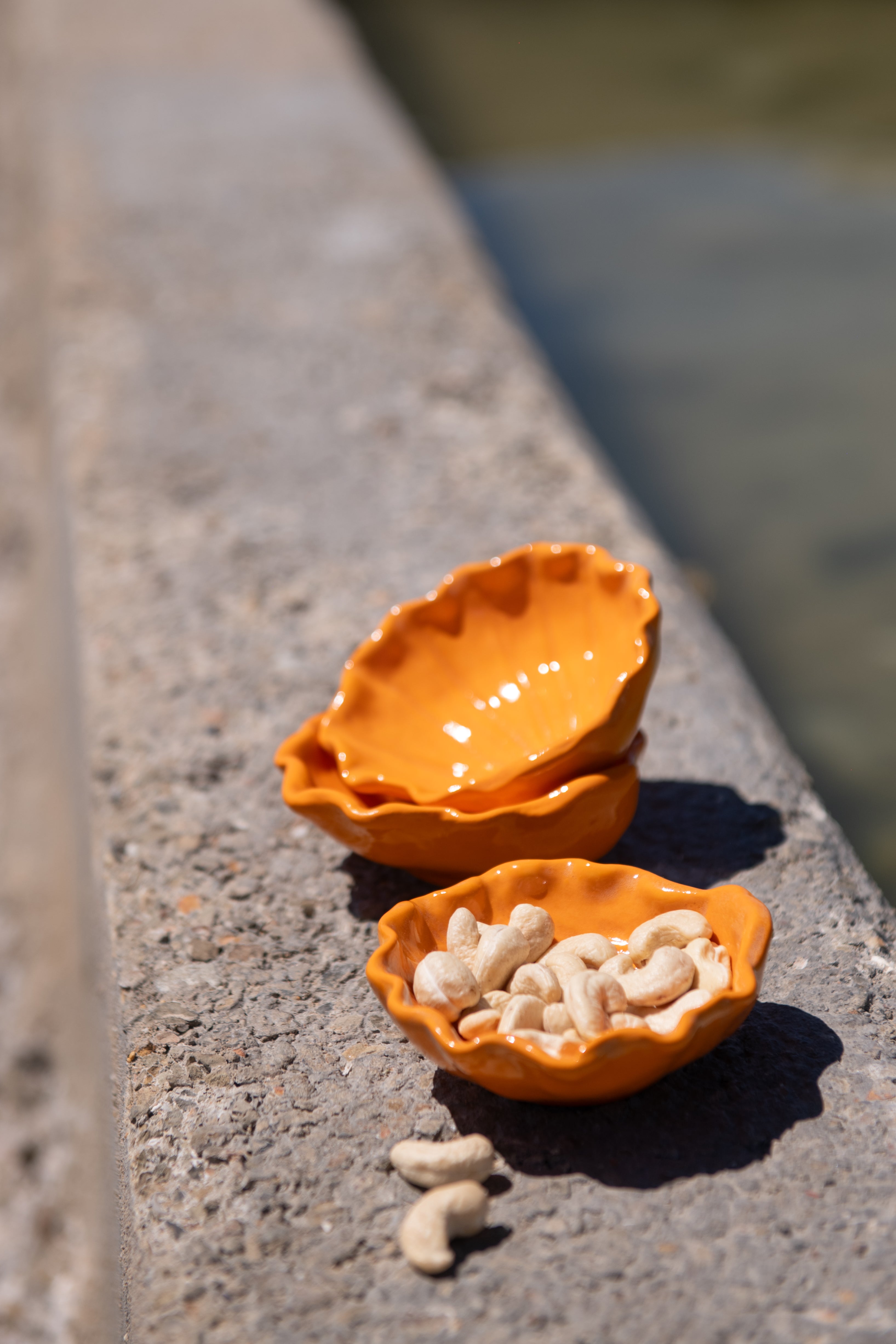 Two orange ceramic bowls on a concrete surface with one containing small white cashews.