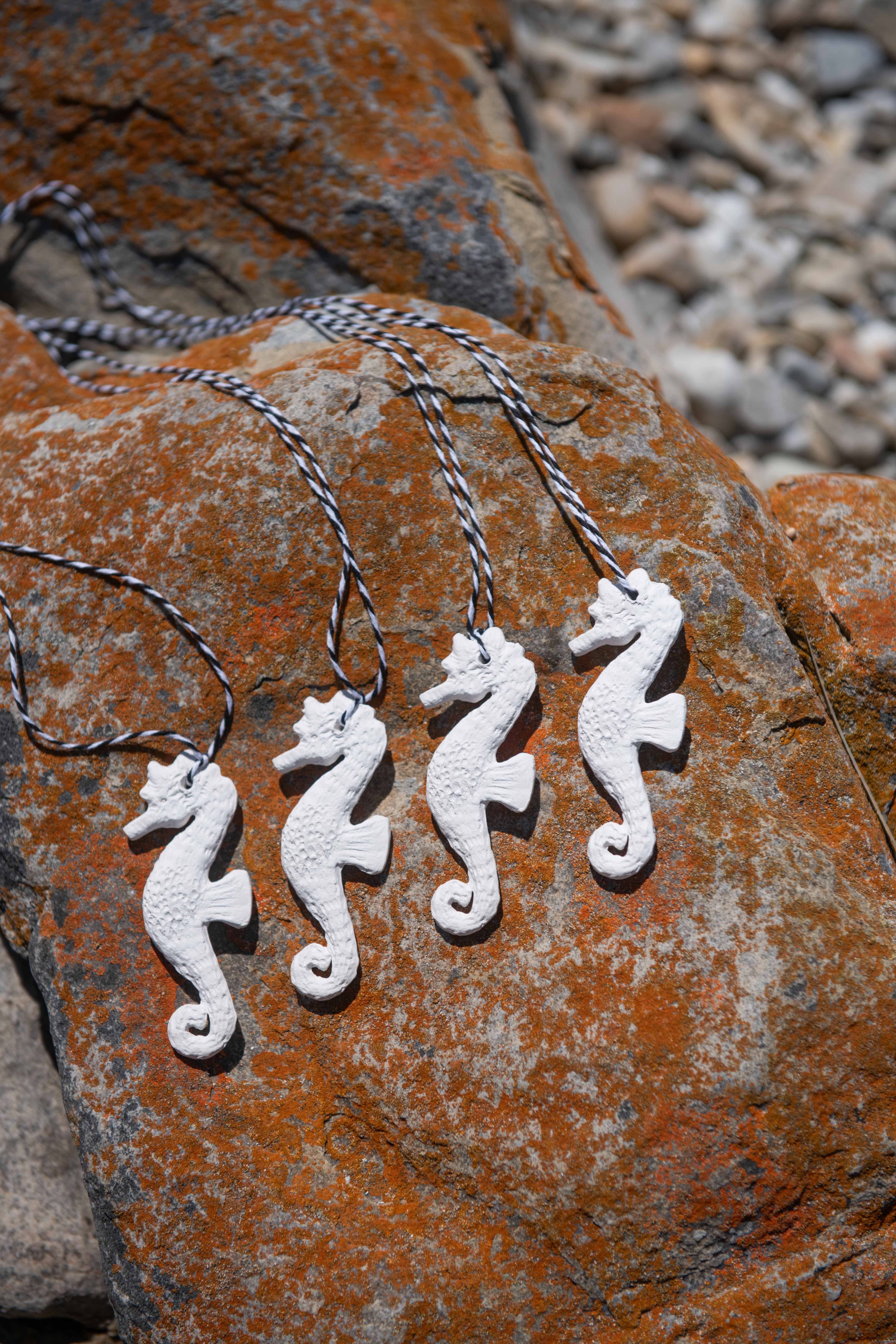 Silver seahorse necklaces on a textured stone surface