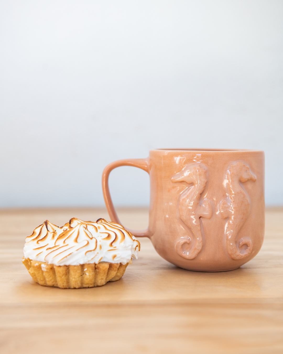 Ceramic mug with seahorse design next to a dessert on a wooden surface