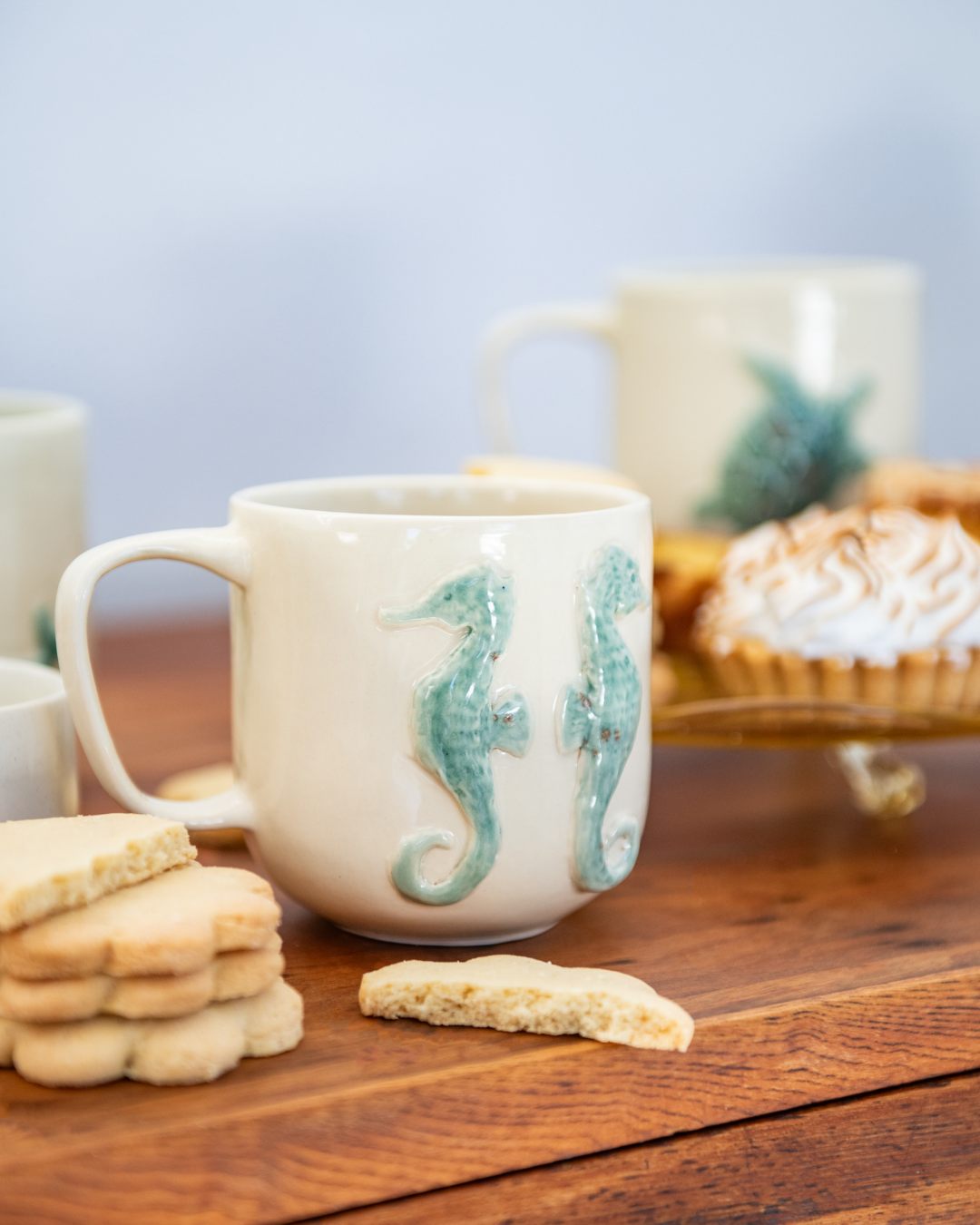 Mug with seahorse design on a wooden table with cookies and pastries.