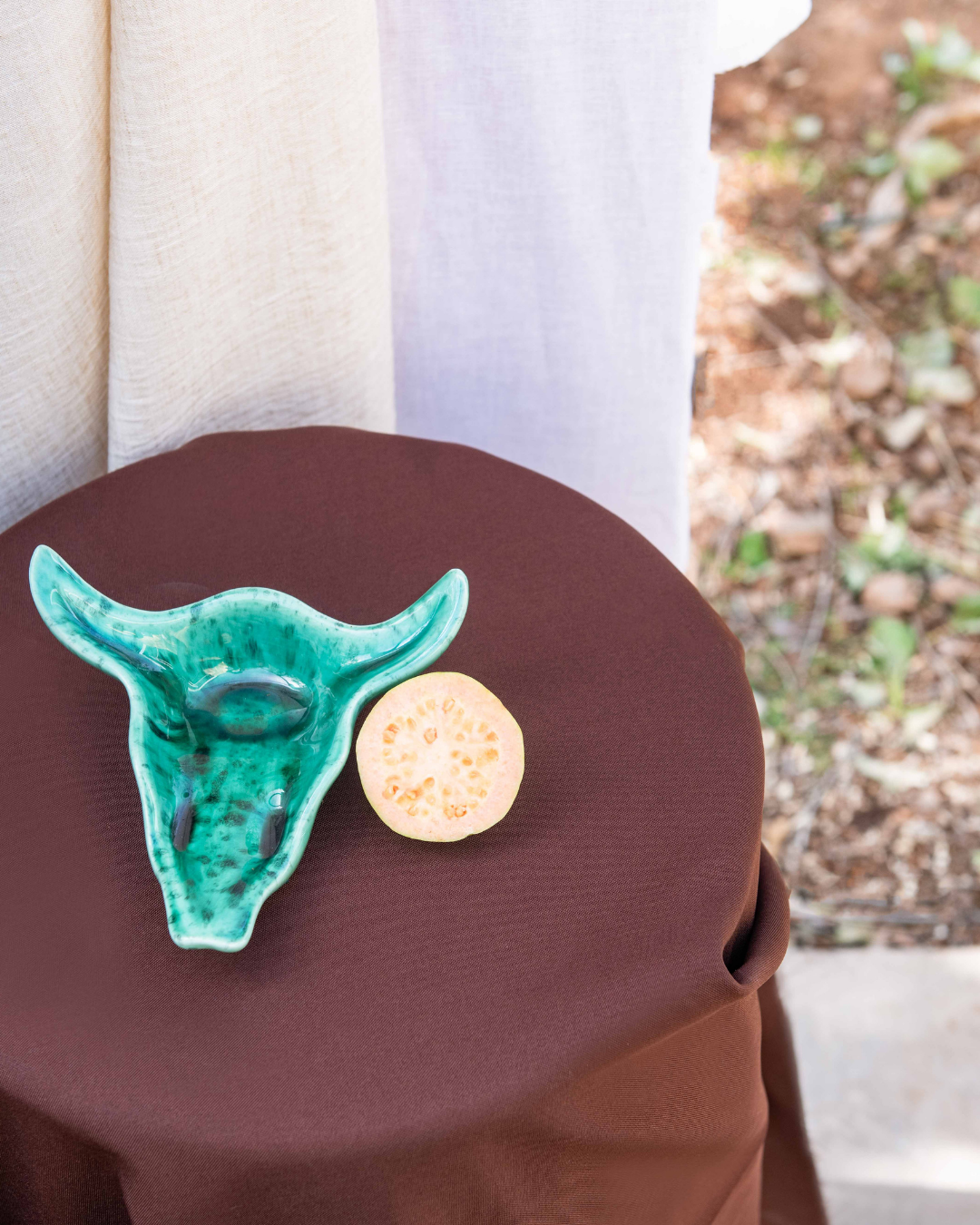 Emerald Green ceramic bull head and fruit on a brown surface with a blurred natural background