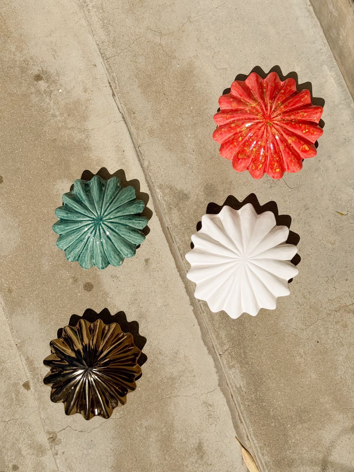 Four decorative metal coasters with different color finishes on a concrete surface.