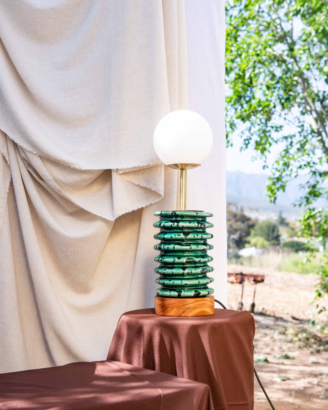 Green Ribbed table lamp with a kiaat foot piece and frosted Glass dome on a brown tablecloth set up in nature