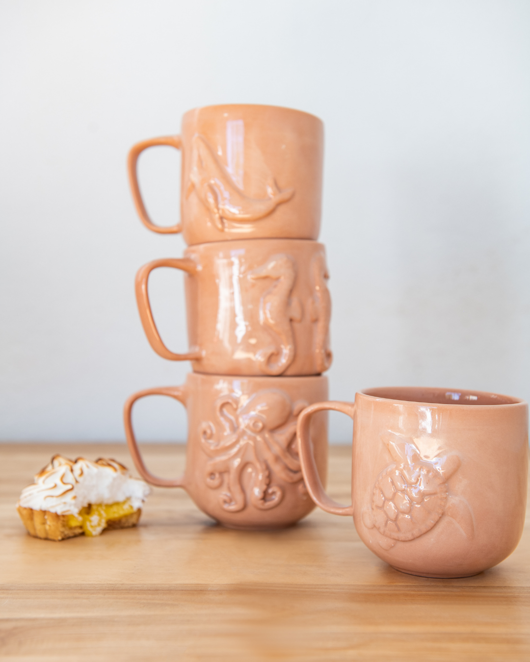 Stack of Terracotta mugs with decorative handles on a wooden surface.
