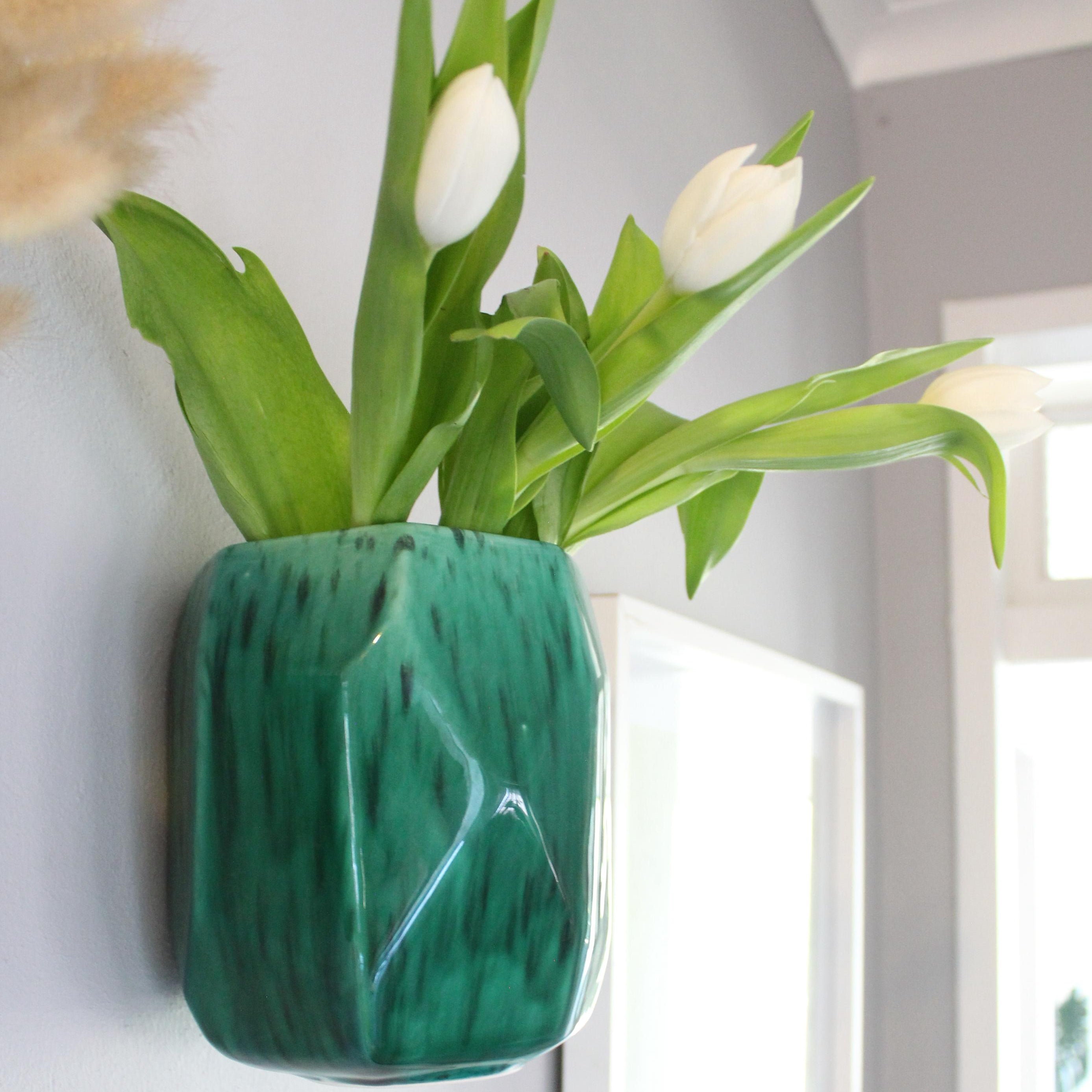 Green marbled wall vase with white tulips against a light gray wall.