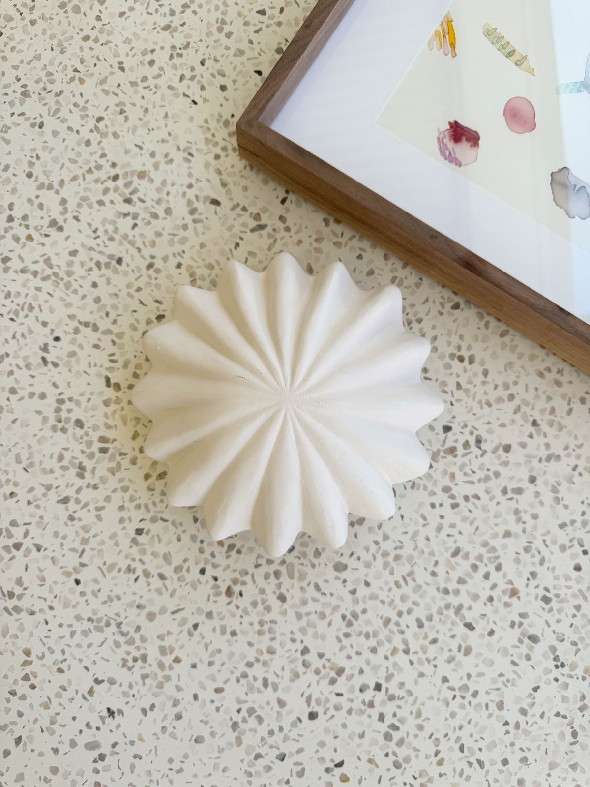 White decorative item on a textured surface with a framed picture in the background