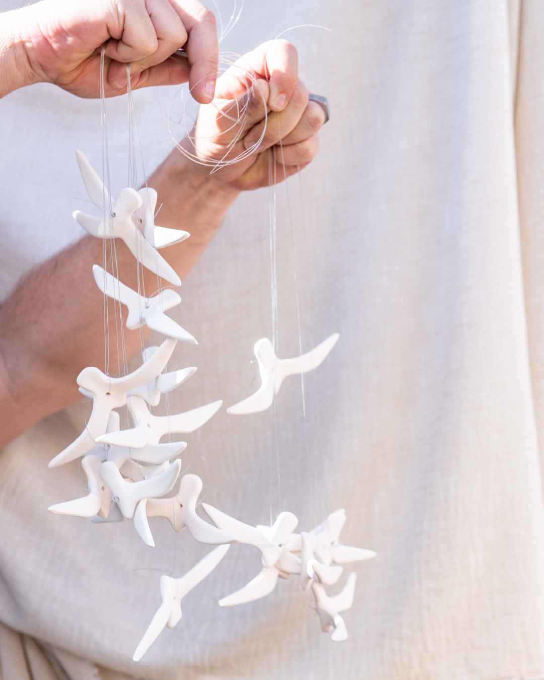 White ceramic birds mobile held by a person against a plain background